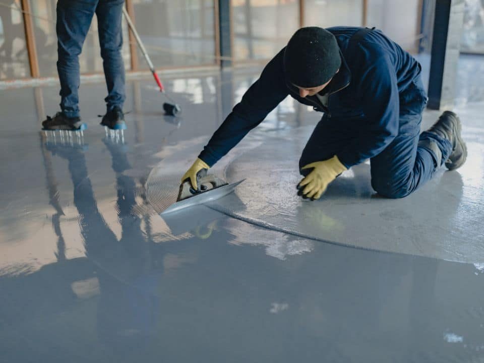 Worker finishing the edge of a gray concrete floor coating application