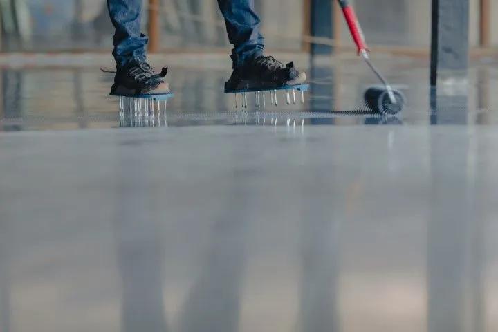 Worker in spiked shoes rolling out epoxy flooring during installation
